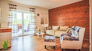 Una sala de estar con pared de madera, un sofá, un sillón estampado, una mesa de centro y una planta en maceta.