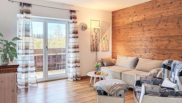 Una sala de estar con una pared de madera, un sofá, una mesa de centro y un ventanal corredizo con cortinas.