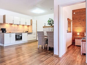 Eine moderne Küche mit weißen Schränken, einem Einbauofen und einer Holz Arbeitsplatte. In der Ecke steht ein Korbstuhl und ein Blumentopf.