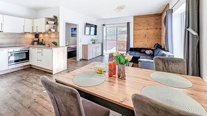 A modern kitchen with white cabinets, a wooden dining table with placemats, and a sofa in the living area. - Beautiful apartment for 4 guests with WIFI, TV, balcony, pets allowed and panoramic view (Klausmen)