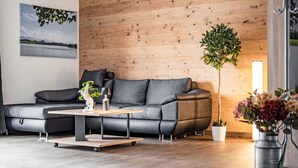 Ein modernes Wohnzimmer mit einer Eckcouch, einem Couchtisch, einer Topfpflanze und einer Wandleuchte.