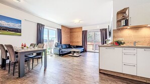 Een modern appartement met een eethoek, een bank, een keuken en een balkon met uitzicht op het omliggende landschap.