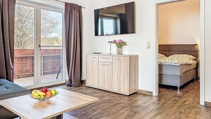 Een moderne kamer met houten vloer, een eettafel met fruit, een kast, een bed en een televisie aan de muur.