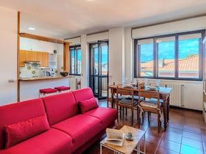 Ein Wohnzimmer mit einem roten Sofa, einem Esstisch mit Stühlen, einer Küchenzeile und großen Fenstern mit Aussicht.