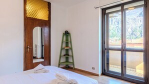 Una camera da letto con un letto, uno scaffale verde, una porta in legno con motivo dorato e una porta scorrevole in vetro che dà su uno spazio all'aperto.