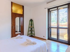 Ein Schlafzimmer mit einem Bett, einem grünen Regal, einer Holztür mit goldenem Muster und einer Glastür, die zu einem Außenbereich führt.