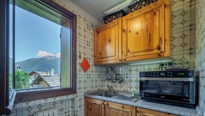 Cuina amb armaris de fusta, forn integrat i finestra amb vista a una muntanya.