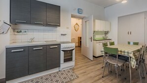 Une cuisine de taille réduite, avec des meubles de couleur sombre, une cuisinière blanche et un coin repas comprenant une table et des chaises.