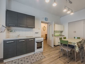 A compact kitchen with dark cabinets, a white stove, and a dining area with a table and chairs. - Lovely apartment for 6 guests with WIFI and TV (Pellizzano)