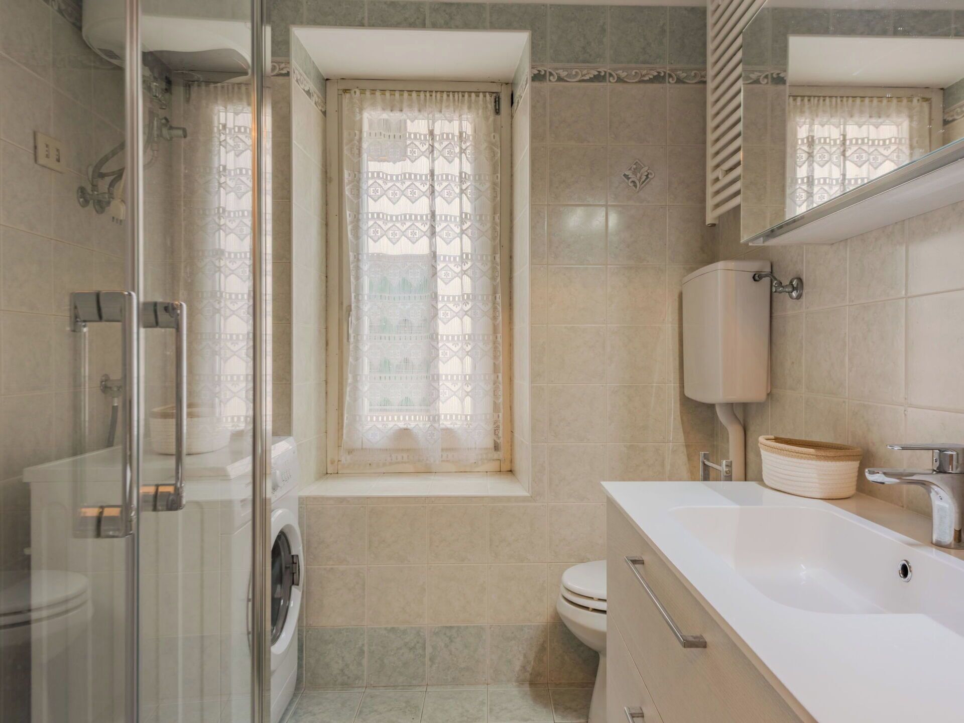Een moderne badkamer met een glazen douchecabine, een ingebouwde wasmachine, een toilet en een wastafel met spiegel.
