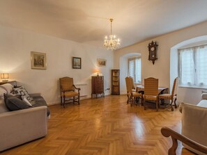 A spacious living room with a herringbone floor, a chandelier, a dining area with a table and chairs, and a large clock on the wall. - Lovely apartment for 6 guests with WIFI and TV (Pellizzano)