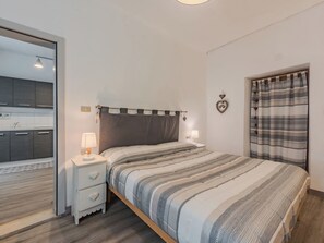 A bedroom with a bed, bedside tables, a mirror, a window with curtains, and a view of the kitchen. - Lovely apartment for 6 guests with WIFI and TV (Pellizzano)