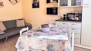 Ett kompakt bostadsutrymme med en soffa, ett matbord med stolar, ett köksområde med skåp och vitvaror samt en väggmonterad tv.