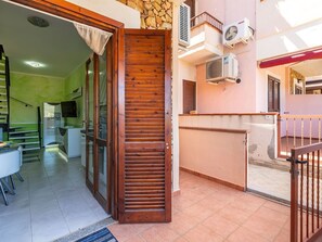 Un intérieur de logement avec une porte en bois, un sol carrelé et un espace cuisine visible à travers une porte en verre.
