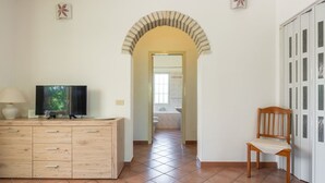 A room with a wooden cabinet, a television, a chair, and a bathroom visible through an arched doorway. - Beautiful private villa for 5 people with A/C, TV, pets allowed and panoramic view (Villasimius)