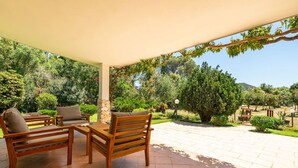 A covered patio with wooden furniture, a stone pillar, and a view of a landscaped garden with trees and a mountain in the background. - Beautiful private villa for 5 people with A/C, TV, pets allowed and panoramic view (Villasimius)