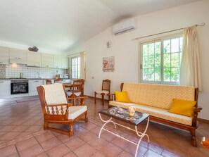 Un salon avec un canapé, des fauteuils, une table basse et, au fond, une cuisine.
