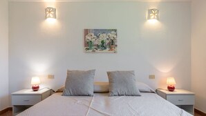 A double bed with a white quilt, two grey pillows, and two bedside tables with lamps. - Beautiful private villa for 5 people with A/C, TV, pets allowed and panoramic view (Villasimius)