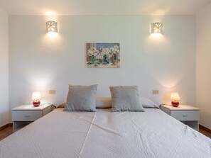 Ein Doppelbett mit weißer Bettdecke, zwei Nachttische mit Lampen und ein Blumenbild an der Wand.