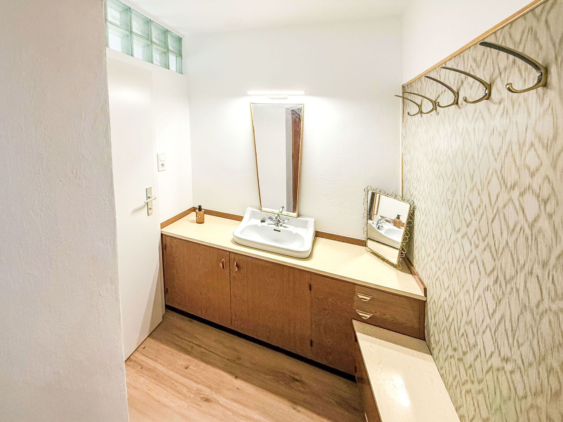 A bathroom with a wooden vanity, a white sink, and a mirror.
