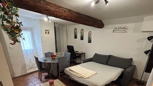 A compact room with a bed, a desk, a chair, and a small table. There is a window with curtains, a ceiling fan, and a wall-mounted shelf with decorative items. - 250m from the Sisteron lake! Fully equipped apartment with office area. (Sisteron)