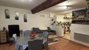 A dining area with a table and chairs, a sofa, a kitchen area with a tiled backsplash, and a wooden ceiling beam. - 250m from the Sisteron lake! Fully equipped apartment with office area. (Sisteron)