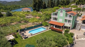 Ein zweistöckiges Gebäude mit Swimmingpool, umgeben von Grünflächen und Bergen.