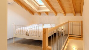 Une chambre avec un plafond en pente, un lit, une petite table et un escalier.
