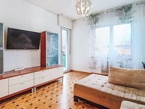 A living room with a sofa, a TV mounted on a cabinet, a patterned window, and a wooden floor. - Beautiful apartment for 6 guests with WIFI, TV and patio (Arco)