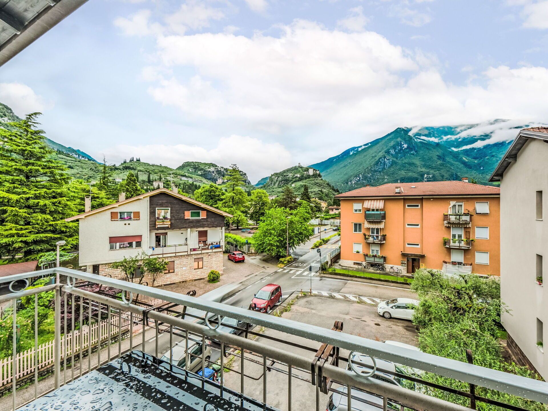 Un quartier résidentiel avec des immeubles de deux étages, une rue bordée de voitures garées et une chaîne de montagnes en arrière-plan.