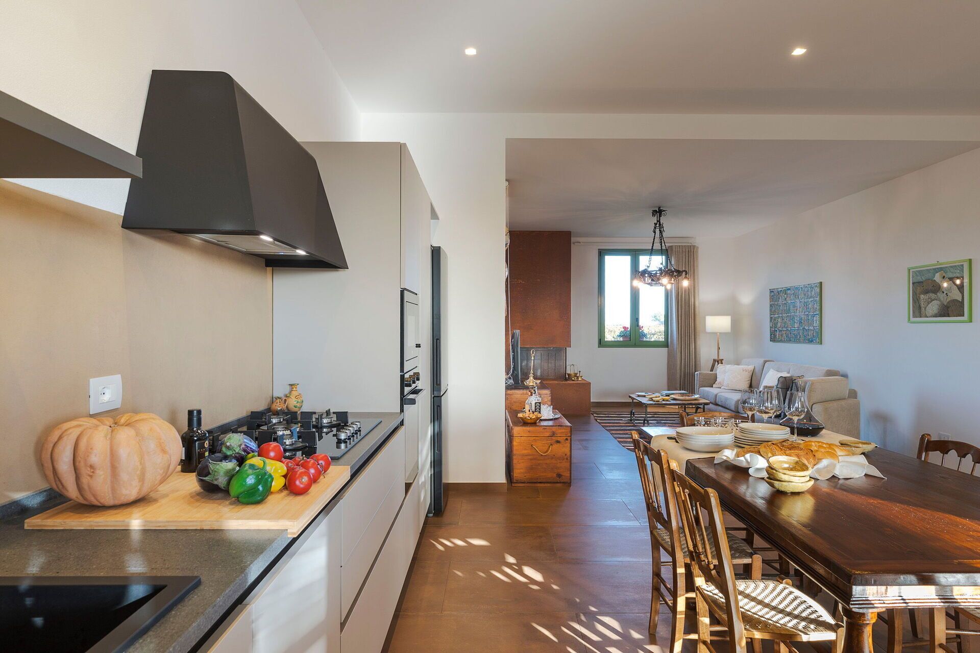 Una cocina moderna con una isla central, un comedor con mesa y sillas de madera, y una sala de estar con sofá y ventana.
