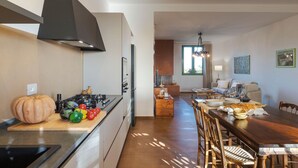 Una cocina moderna con una isla central, un comedor con mesa y sillas de madera, y una sala de estar con sofá y ventana.