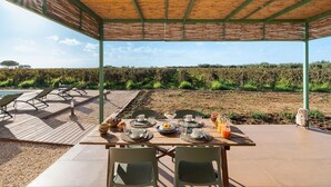 Un área de comedor al aire libre con vistas a un viñedo, mesas y sillas de madera, y una estructura de pérgola.