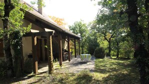 A covered outdoor area with a table and chairs, surrounded by trees and a building. - Bright country house with open kitchen (Saint-Jean-de-Laur)