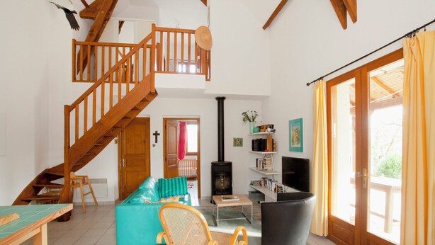 A spacious living area with a wooden staircase, a sofa, a TV, and a fireplace. - Bright country house with open kitchen (Saint-Jean-de-Laur)