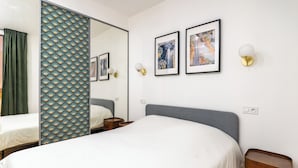 Ein Hotelzimmer mit einem großen Bett, einem Nachttisch, einem Spiegel und zwei gerahmten Kunstwerken an der Wand.