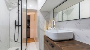 Ein modernes Badezimmer mit einer gläsernen Dusche, einem weißen Waschbecken auf einer Holzkommode und einem großen Spiegel darüber.