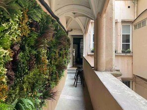 A narrow corridor with a vertical garden wall, a bench, and a view of a building with windows and a door. - Rue Mercière, Terrace, Hypercentre, Lyon (Lyon)