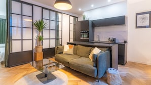 Ein modernes Wohnzimmer mit einer Couch, einem Glastisch und einer Küchenzeile inklusive Backofen und Mikrowelle.