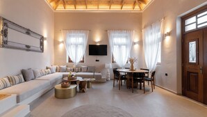 Un salon spacieux avec un plafond haut, un ensemble de canapés, une table à manger avec des chaises et un téléviseur fixé au mur.