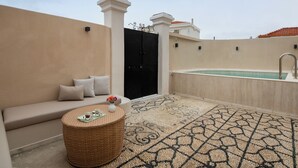 Une terrasse sur le toit avec un canapé beige, une table ronde en osier sur laquelle repose un plateau, et un tapis à motifs.
