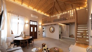 Un vaste espace de vie doté d’un haut plafond, d’une table à manger, de canapés et d’un escalier menant à un niveau supérieur.