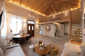 A spacious living area with a high ceiling, a dining table, sofas, and a staircase leading to an upper level. - Archontiko Residence (Koskinou)