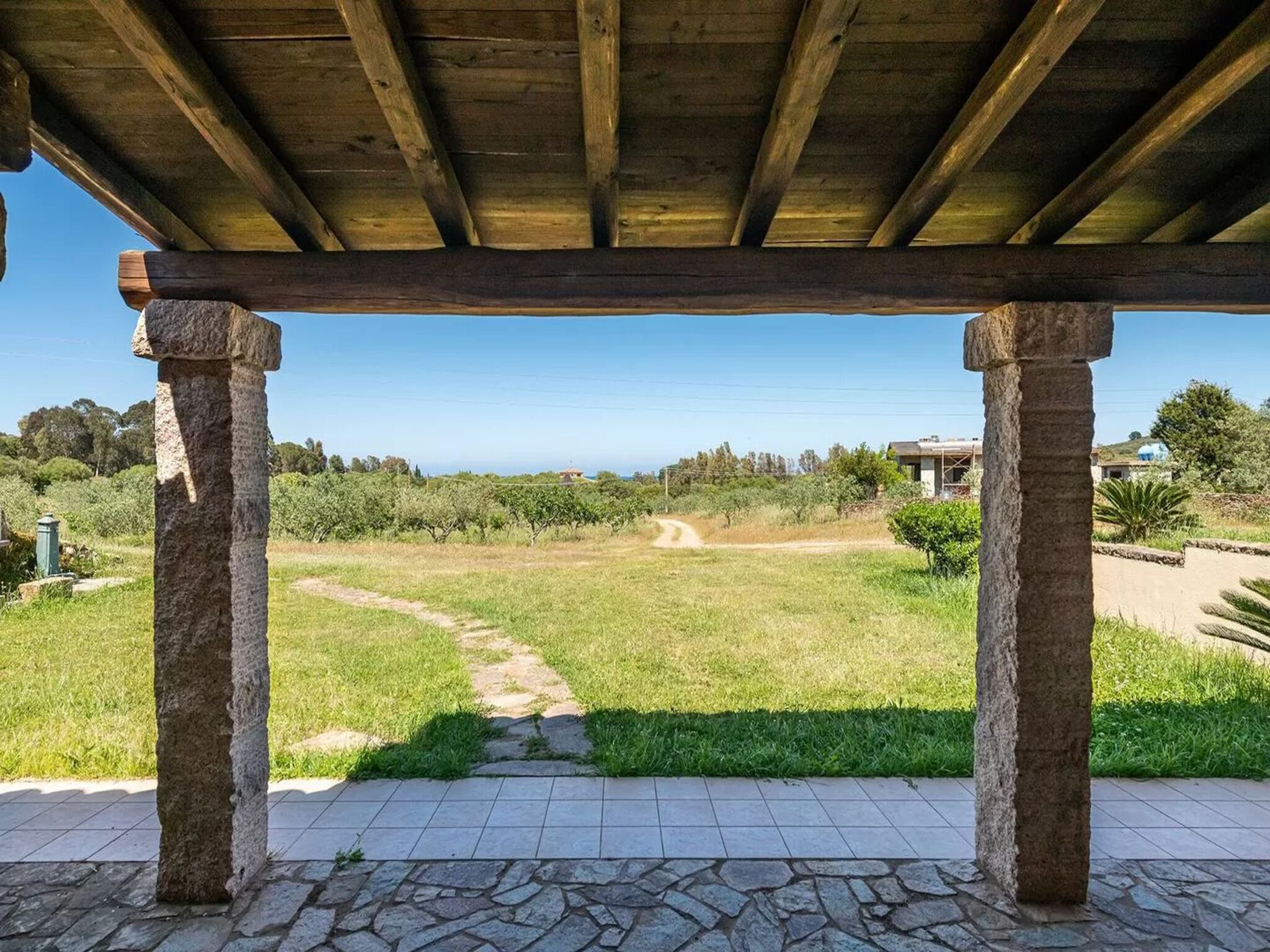 Un espacio al aire libre cubierto con columnas de piedra, un camino empedrado y vistas a un campo cubierto de césped y edificios a la distancia.