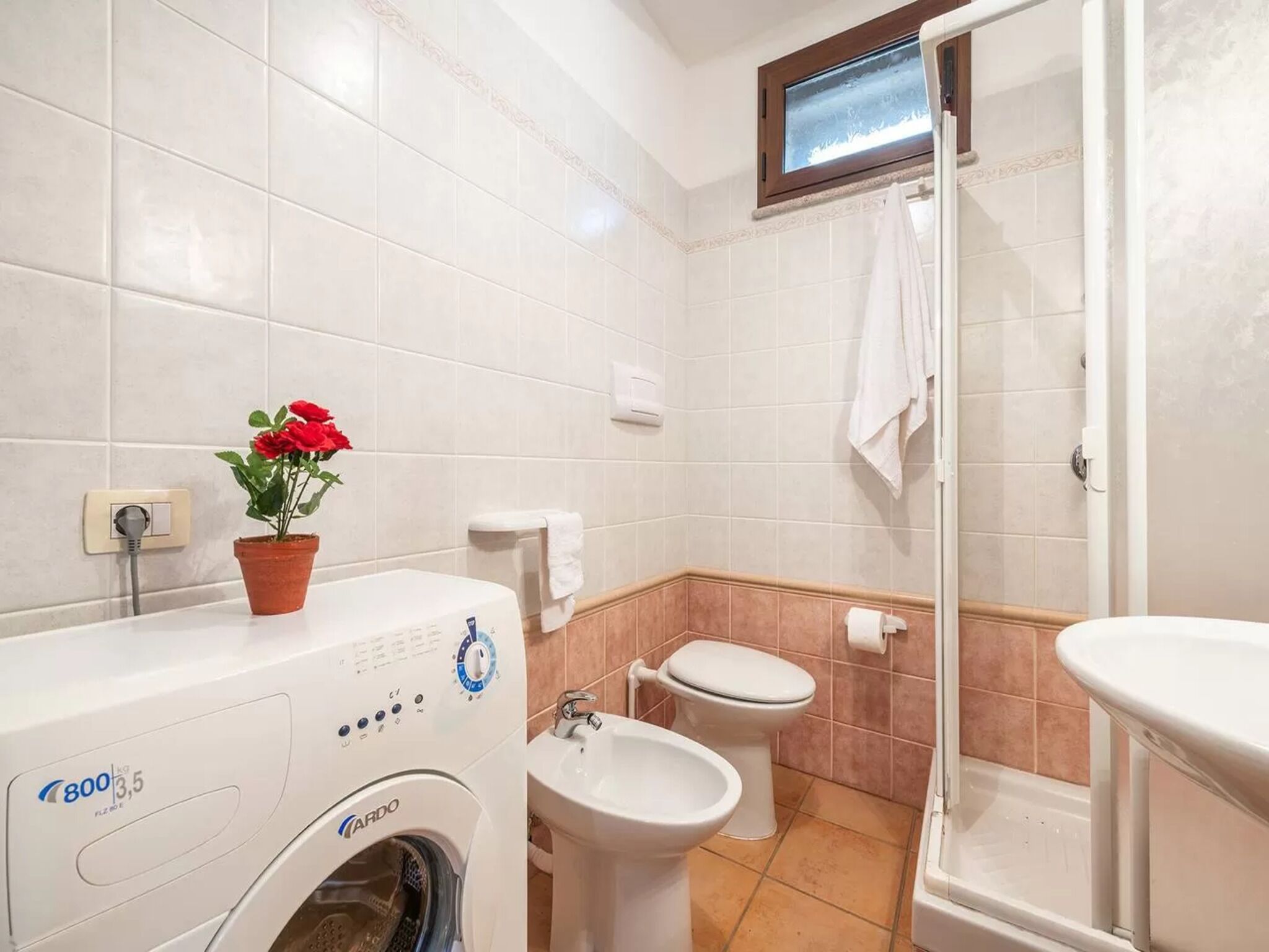 A bathroom with a washing machine, toilet, bidet, and a small window.