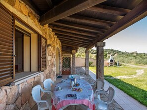 Une terrasse extérieure avec une table dressée pour les repas, des murs en pierre, des poutres en bois et une vue sur la campagne.