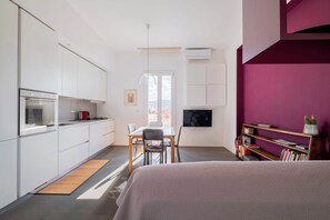 Een kleine kamer met een kitchenette, een eethoek en een bed.