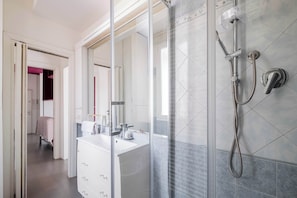 Een moderne badkamer met een douchecabine van glas, een witte wastafel en een spiegel.
