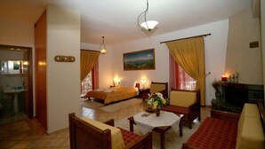 A hotel room with a bed, a sitting area with a table and chairs, a fireplace, and a painting on the wall.