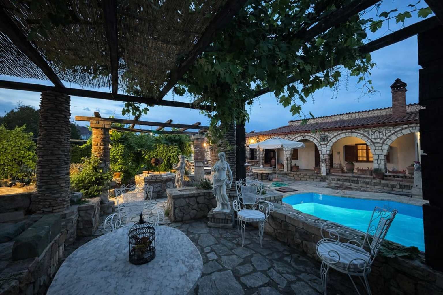 A stone patio with a pool, outdoor seating, and a pergola.